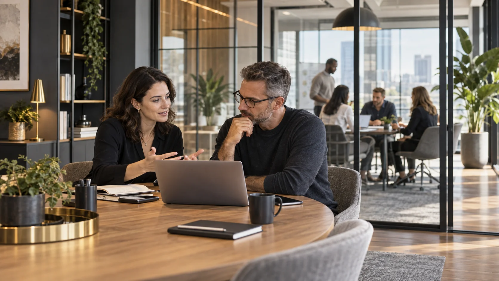 A consultant and business owner reviewing work together in an office, with colleagues collaborating in the background